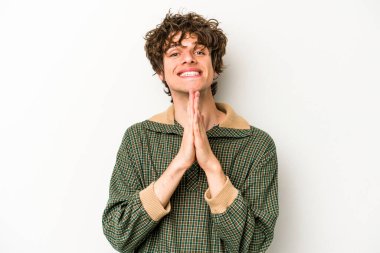 Beyaz arka planda izole edilmiş genç beyaz bir adam el ele tutuşup, ağız kenarında dua ediyor, kendinden emin..