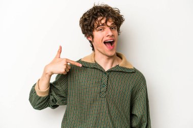 Beyaz arka planda yaşayan beyaz tenli genç bir adam gömlek fotokopi alanını gösteriyor, gururlu ve kendinden emin.