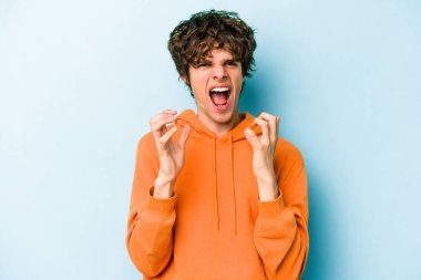 Mavi arka planda izole edilmiş genç beyaz adam gergin elleriyle çığlık atıyor..