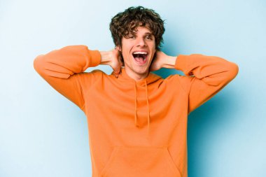 Mavi arka planda izole edilmiş genç beyaz adam kollarını uzatıyor, rahat bir konumda..