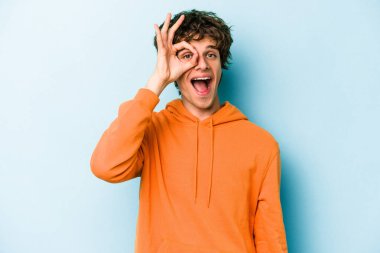 Kafkasyalı genç adam mavi arka planda izole edildi. Heyecanlı görünüyor..