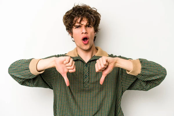 Beyaz arka planda izole edilmiş genç beyaz bir adam baş parmağını aşağı gösteriyor ve hoşlanmadığını ifade ediyor..