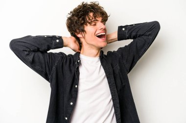 Beyaz arka planda izole olmuş genç beyaz bir adam kendini güvende hissediyor, elleri başının arkasında..