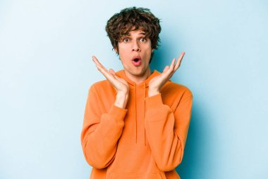 Kafkasyalı genç adam mavi arka planda izole edildi. Şaşırdı ve şok oldu..