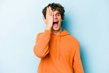 Mavi arka planda izole edilmiş genç beyaz adam yüzünün yarısını palmiye ile kaplayarak eğleniyor..