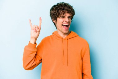 Mavi arka planda izole edilmiş genç beyaz adam boynuzlarını devrim konsepti olarak gösteriyor..