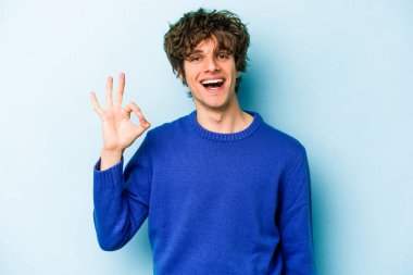 Kafkasyalı genç adam mavi arka planda izole edilmiş neşeli ve kendinden emin..