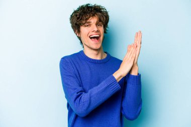 Kafkasyalı genç adam mavi arka planda izole edilmiş enerjik ve rahat hissediyor, ellerini ovuşturuyor kendinden emin.