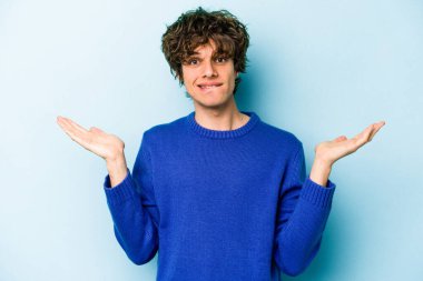 Kafkasyalı genç adam mavi arka planda izole edilmiş. Kafası karışmış ve omuz silkiyor. Kopya alanını tutmak için..