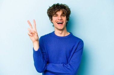 Mavi arka planda izole edilmiş genç beyaz adam iki numarayı parmaklarıyla gösteriyor..