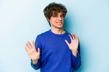 Mavi arka planda izole edilmiş genç beyaz adam tiksinti belirtisi gösteren birini reddediyor..