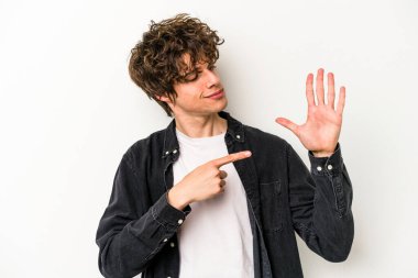 Beyaz arka planda izole edilmiş genç beyaz bir adam gülümseyerek beş numarayı parmaklarıyla gösteriyor..