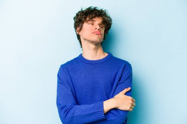 Mavi arka planda izole edilmiş genç beyaz adam tekrarlanan bir görevden yoruldu..