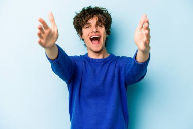 Mavi arka planda izole edilmiş genç beyaz adam kameraya sarıldığı için kendinden emin hissediyor..