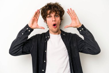 Beyaz arka planda izole olmuş genç beyaz bir adam zaferi veya başarıyı kutluyor, şaşırıyor ve şok oluyor..