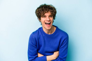 Kafkasyalı genç adam mavi arka planda izole edilmiş gülüyor ve eğleniyor..