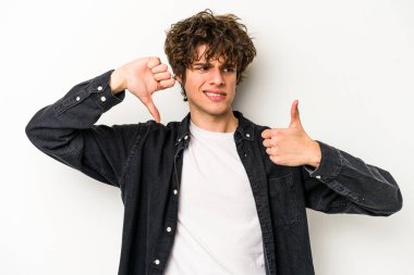 Beyaz arka planda izole edilmiş genç beyaz bir adam baş parmaklarını aşağı ve yukarı kaldırıyor, zor seçim konsepti