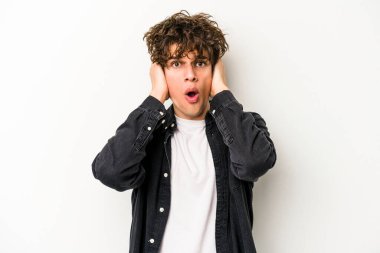 Beyaz arka planda izole edilmiş genç beyaz bir adam kulakları kulaklarıyla kapatıyor ve çok ses duymamaya çalışıyor..