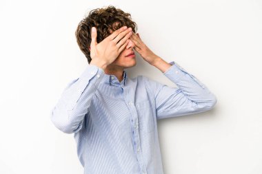 Beyaz arka planda izole edilmiş genç beyaz bir adam elleriyle gözlerini kapatmaktan korkuyor..