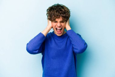 Kafkasyalı genç adam mavi arka planda izole edilmiş kulakları kulaklarıyla kapatıyor çok fazla ses duymamaya çalışıyor..