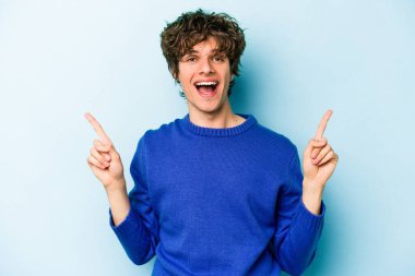 Mavi arka planda izole genç beyaz adam işaret iki ön parmakları boş bir boşluk gösteren.
