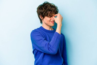 Kafkasyalı genç bir adam mavi arka planda izole edilmiş, başı ağrıyor, yüzüne dokunuyor..