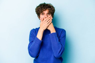 Kafkasyalı genç adam mavi arka planda izole edilmiş ağzı kapalı ve elleri endişeli görünüyor..