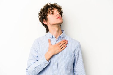 Beyaz arka planda izole edilmiş genç beyaz adam yemin ediyor, elini göğsüne koyuyor..