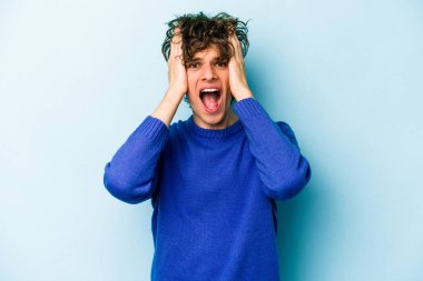 Genç beyaz adam mavi arka planda izole edilmiş bağırıyor, çok heyecanlı, tutkulu, bir şeyden memnun..