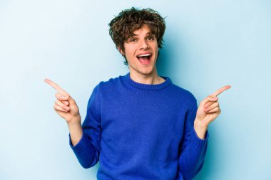 Mavi arka planda izole edilmiş genç beyaz adam farklı kopya alanlarını gösteriyor, birini seçiyor, parmaklarıyla gösteriyor.