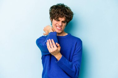 Kafkasyalı genç adam mavi arka planda izole edilmiş dirsek masajı yapıyor, kötü bir hareketin ardından acı çekiyor..