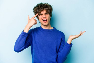 Kafkasyalı genç adam mavi arka planda izole edilmiş ve elinde bir ürün tutuyor..