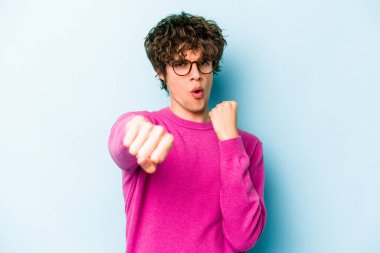 Kafkasyalı genç bir adam mavi arka planda izole edilmiş. Yumruk atıyor, sinirleniyor, kavga ediyor, kavga ediyor..