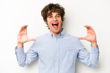 Beyaz arka planda izole edilmiş genç beyaz bir adam elinde avuç içi bir şeyle kameraya sunuyor..