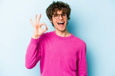 Kafkasyalı genç bir adam mavi arka planda izole edilmiş bir şekilde göz açıp kapayana kadar iyi bir el hareketi yapıyor..