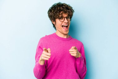 Mavi arka planda izole edilmiş genç beyaz adam parmaklarıyla ön tarafı işaret ediyor..