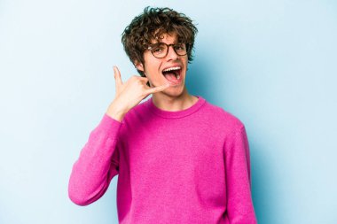 Mavi arka planda izole edilmiş genç beyaz adam parmaklarıyla bir cep telefonu hareketi gösteriyor..