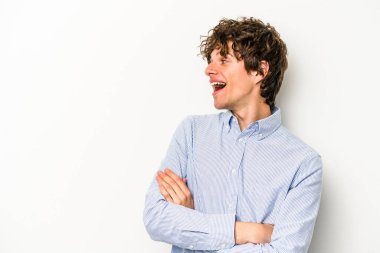 Beyaz arka planda izole edilmiş genç beyaz adam kollarını kavuşturarak gülümsüyor..