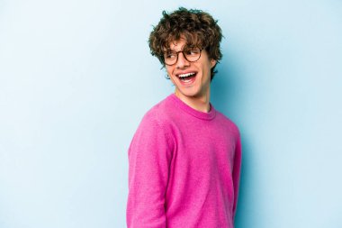 Mavi arka planda soyutlanmış genç beyaz bir adam gülümsüyor, neşeli ve keyifli görünüyor..