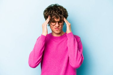 Genç beyaz adam mavi arka planda izole edilmiş tapınaklara dokunuyor ve başı ağrıyor..