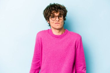 Mavi arka planda izole edilmiş genç beyaz adam omuzlarını silkeliyor ve gözleri açık..