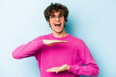 Mavi arka planda izole genç beyaz adam iki eliyle bir şey tutuyor, ürün sunumu..