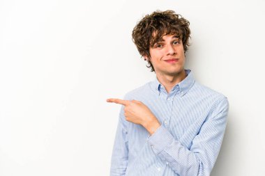 Beyaz arka planda izole edilmiş genç beyaz bir adam gülümsüyor ve boş alanda bir şeyler gösteriyor..