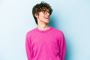 Kafkasyalı genç adam mavi arka planda izole edilmiş rahat ve mutlu bir şekilde gülüyor, boynunda dişlerini gösteriyor..