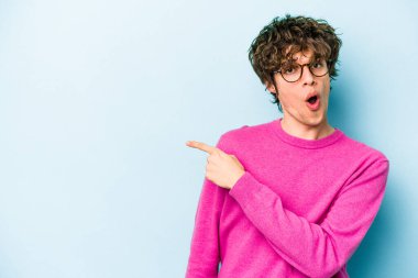 Kafkasyalı genç adam mavi arka plan noktalarında izole edilmiş başparmak uzakta, gülüyor ve kaygısız.