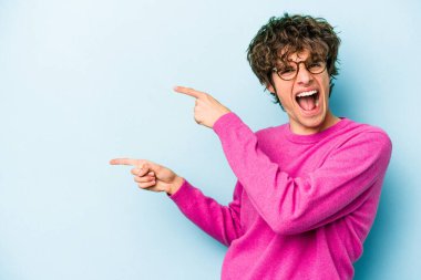 Kafkasyalı genç adam mavi arka planda izole edilmiş. İşaret parmağıyla işaret ettiği için heyecanlı..