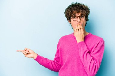 Mavi arka planda izole edilmiş genç beyaz adam yan tarafı işaret ediyor.