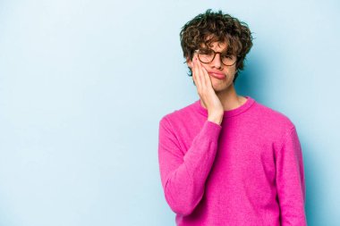 Mavi arka planda izole edilmiş, üzgün ve dalgın hisseden, kopyalama alanına bakan genç beyaz bir adam..