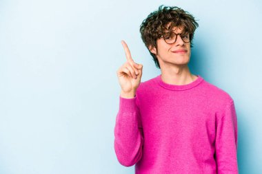 Mavi arka planda izole edilmiş genç beyaz adam bir numarayı parmağıyla gösteriyor..