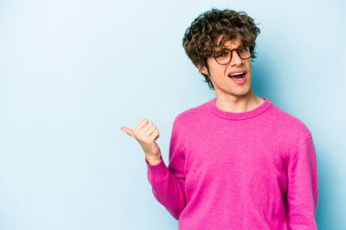 Mavi arka planda izole edilmiş genç beyaz adam işaret parmağıyla fotokopi alanını işaret ederek şok oldu..